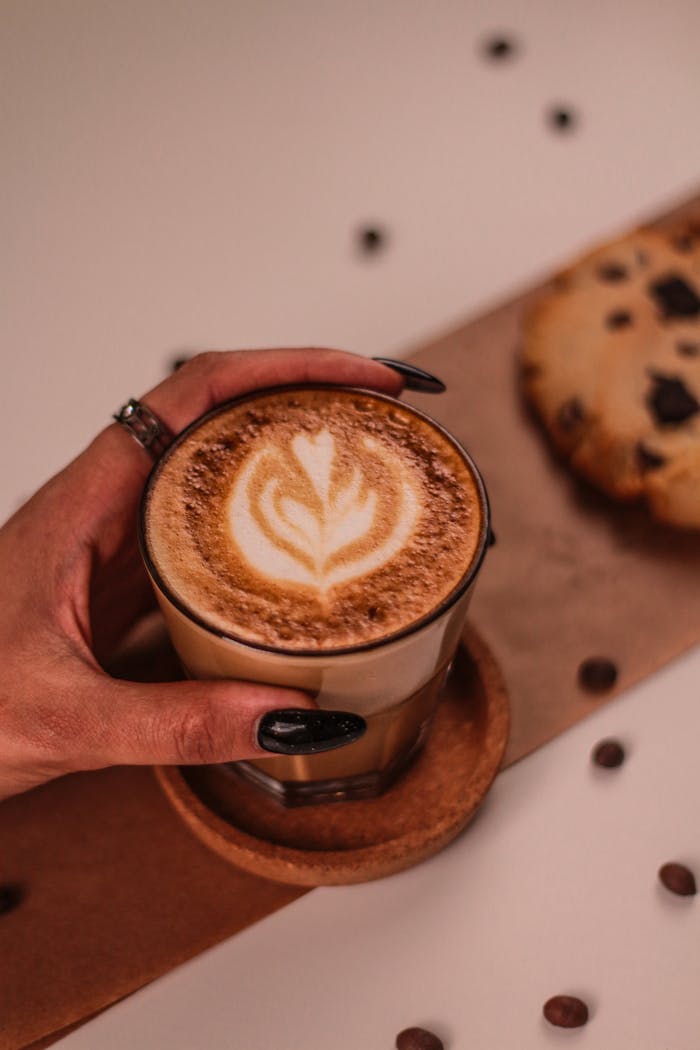 A cup of latte with art and a chocolate chip cookie, perfect for coffee enthusiasts.